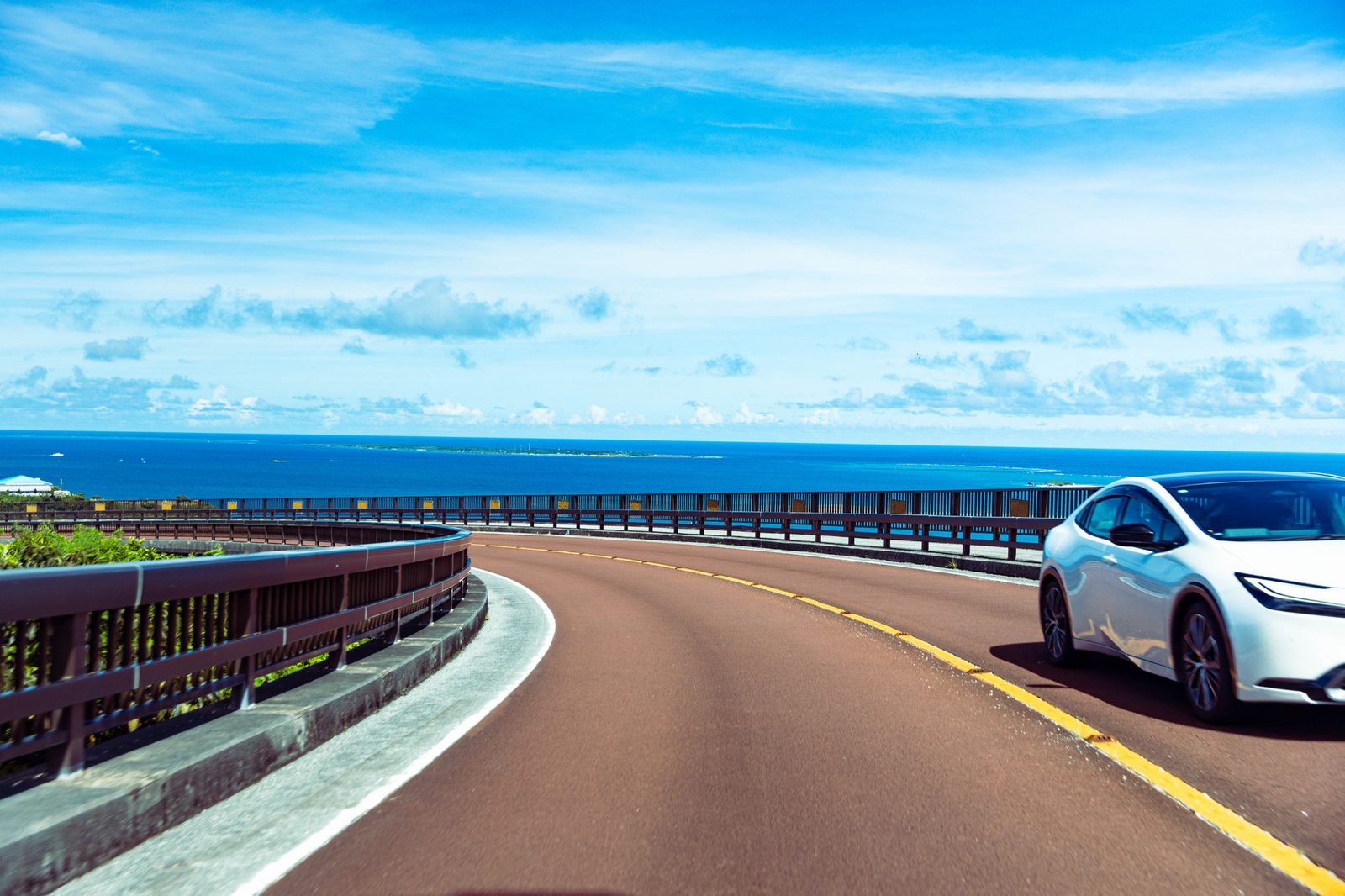 沖縄の海沿いの道をドライブする車（イメージ）